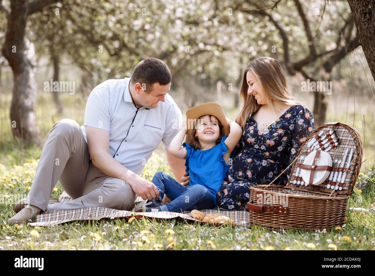 Portrait of happy family on picnic. pregnant Mom, dad and daughter sitting  in spring blooming park. Young family spending time together on vacation  Stock Photo - Alamy