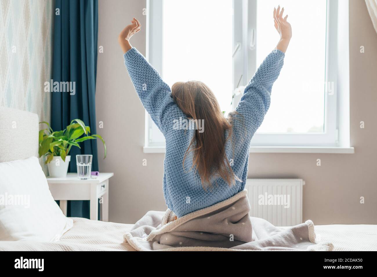 Young long-haired woman outstretching her arms sitting on the bed after ...