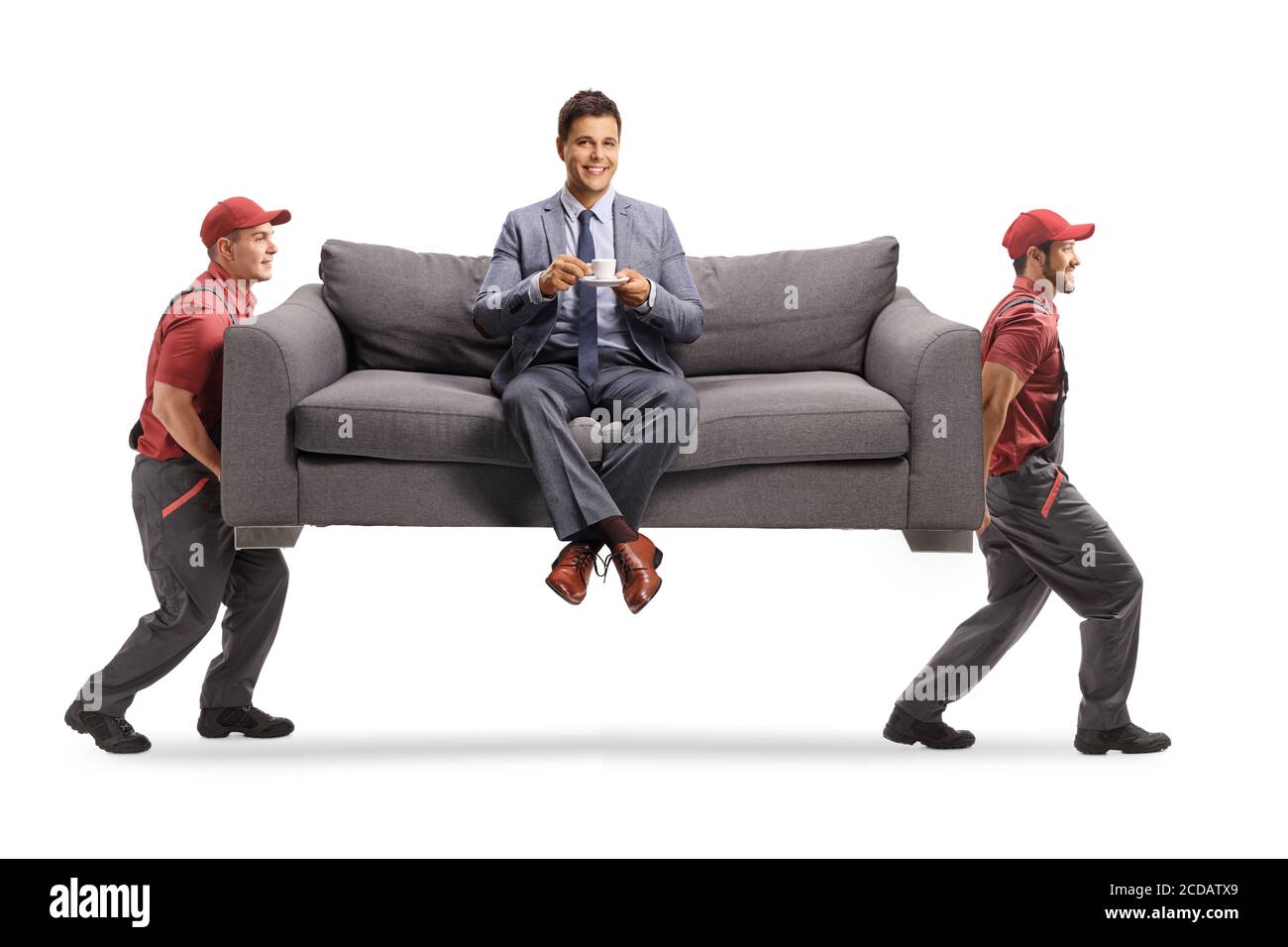 Man in elegant clothes sitting on a sofa with a cup of coffee while two movers are carrying the sofa in a van isolated on white background Stock Photo