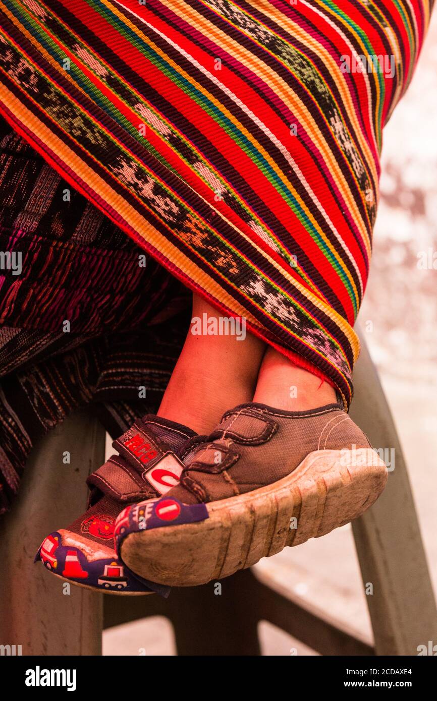 A young boy's feet stick out of his mother's tzute cloth as he sleeps on her back in the market in Chichicastenango, Guatemala. Stock Photo