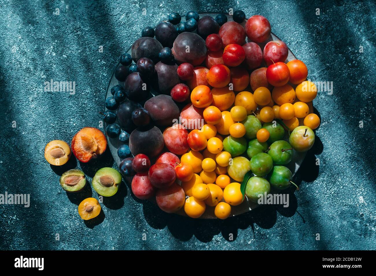 Multicolored plums on a plate are laid out by color. Stock Photo