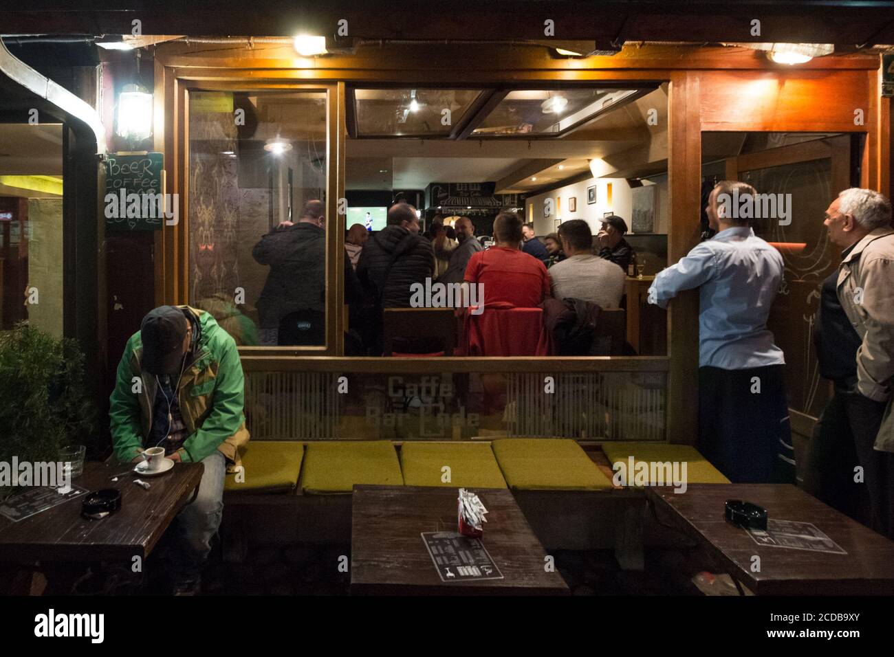 SARAJEVO, BOSNIA - APRIL 15, 2017: Man sleeping in a bar while others are standing watching a football match on TV in a bar and cafe of Bascarsija dis Stock Photo