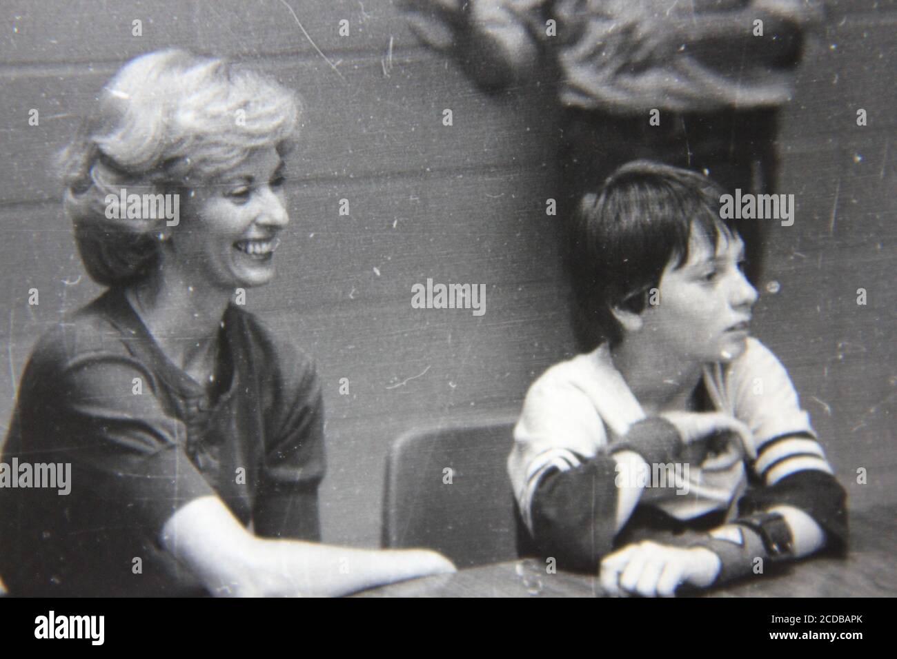 Fine 1970s vintage black and white photography of a beautiful woman smiling and sitting next to her son at a table. Stock Photo