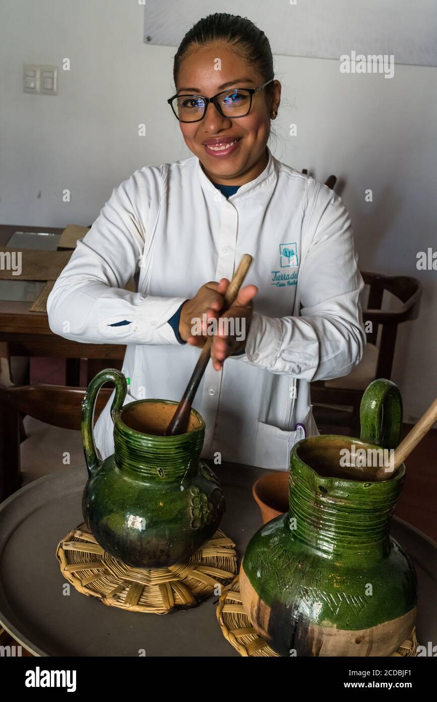 This waitress is preparing Oaxacan hot chocolate, mixing it by spinning a carved wooden molinillo in the traditional green ceramic pitcher of hot chol Stock Photo