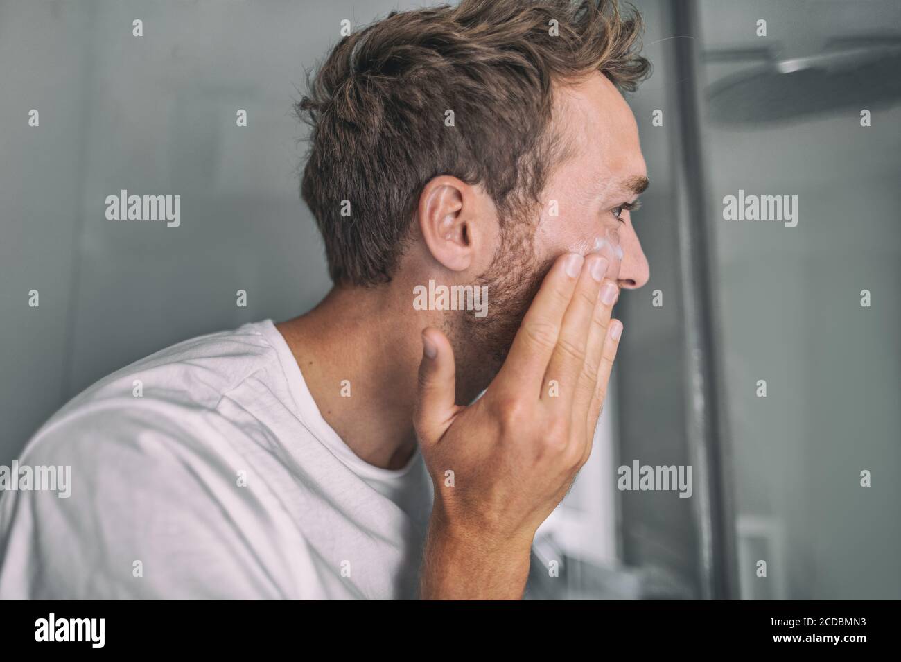 Skin care young man putting face cream for facial acne treatment in home bathroom. Men beauty skincare lifestyle Stock Photo