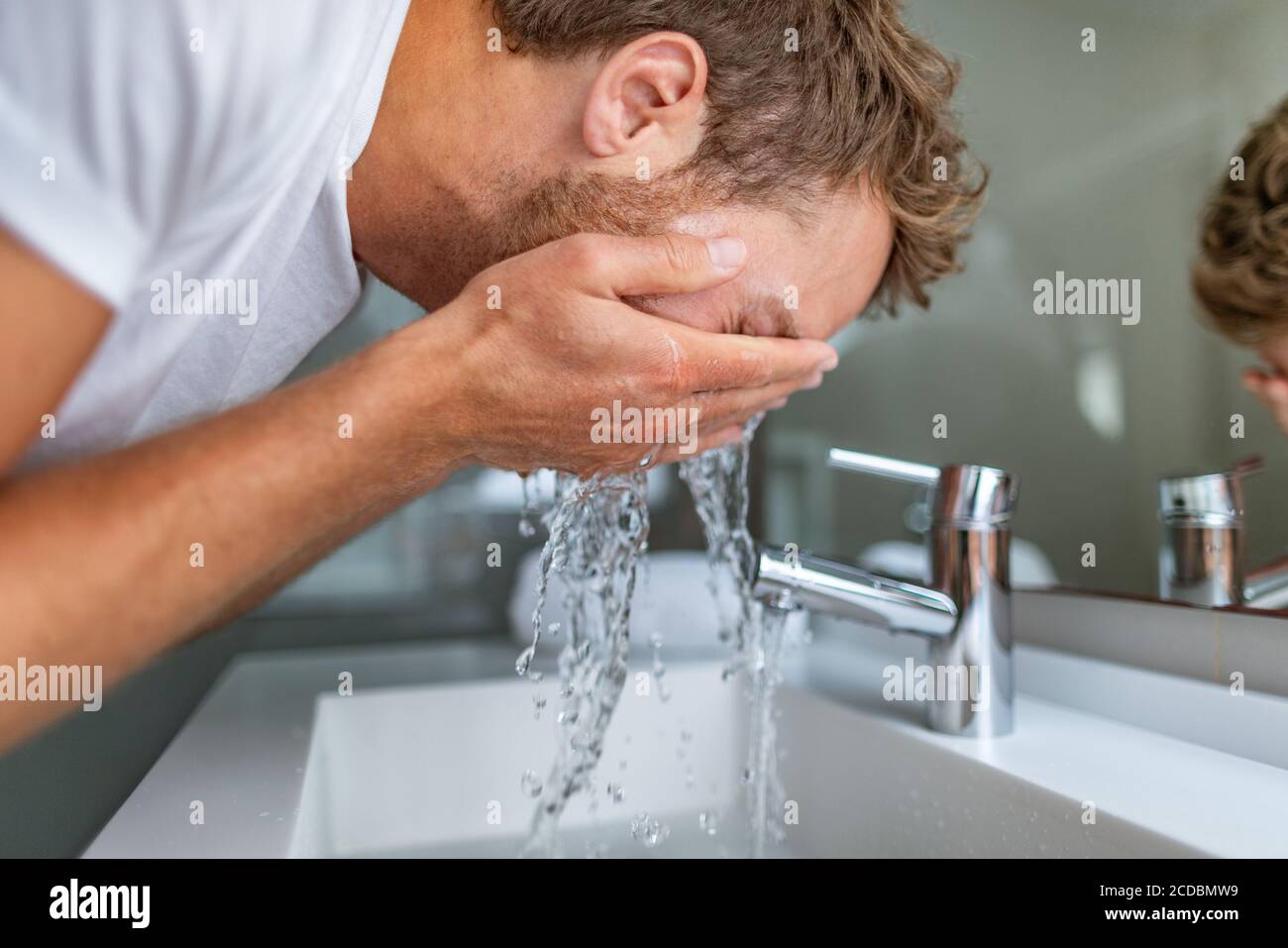 Face wash man in bathroom washing cleansing for acne facial treatment in sink splashing cold water onto face. Men beauty skincare lifestyle Stock Photo