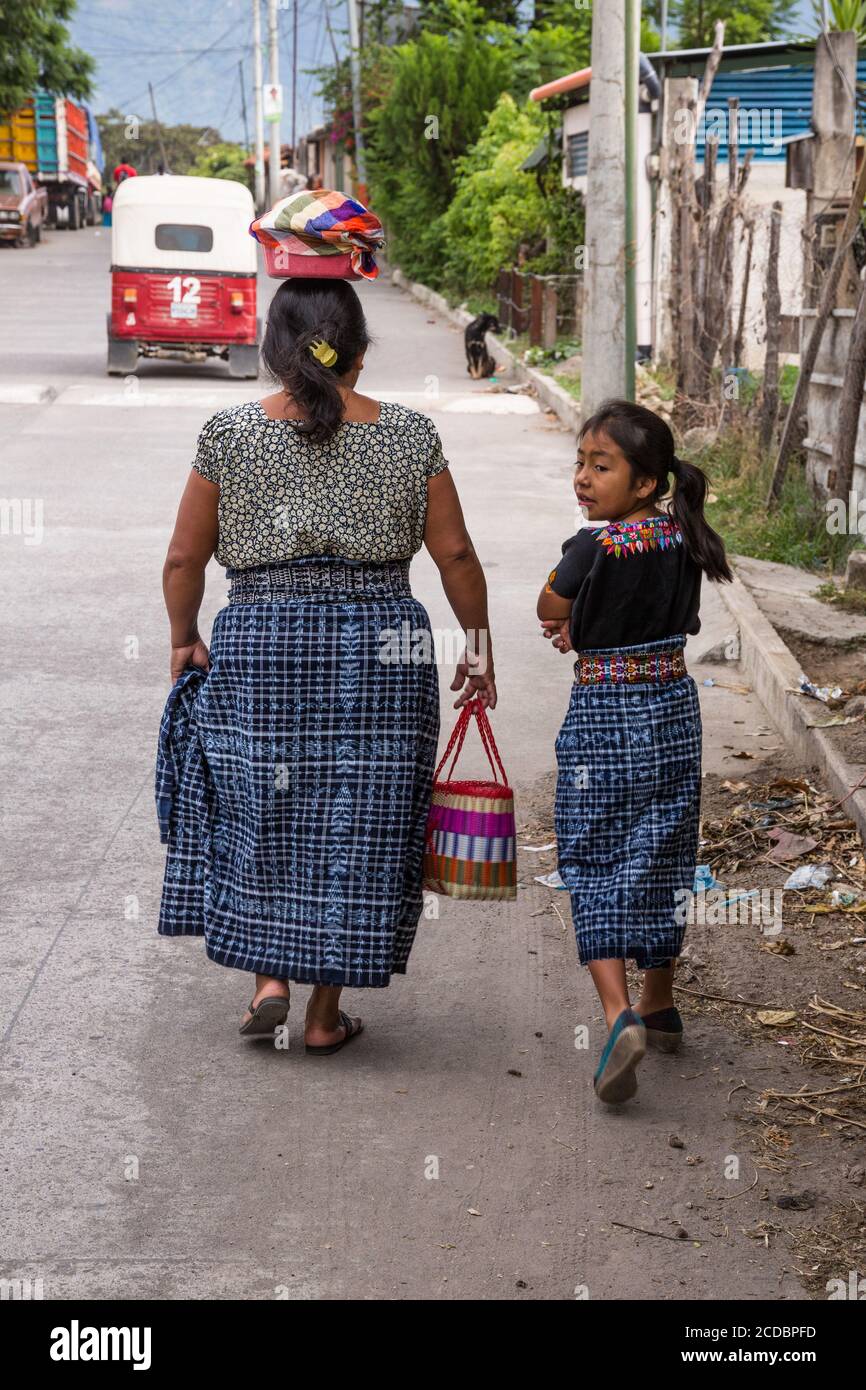 A Mayan mother and daughter in traditiional dress walk towards home in San Pedro la Laguna, Guatemala.  The woman balances a bowl of fresh tortillas o Stock Photo