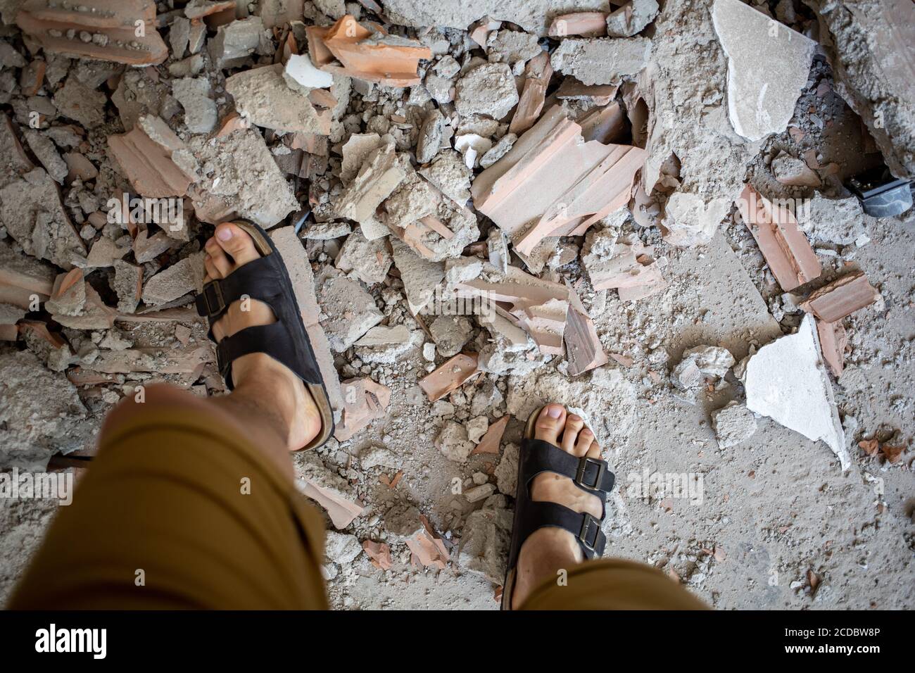 male feet in sandals over pile of building trash Stock Photo