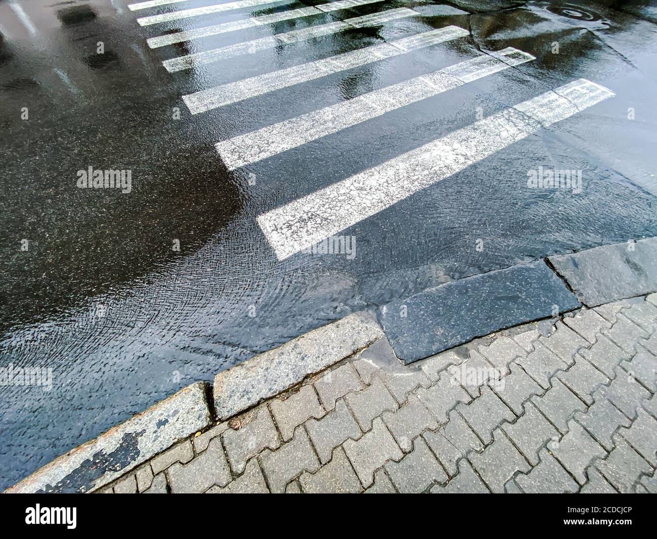 white zebra pedestrian crossing after heavy rain. rainy background with water flows and sky reflections Stock Photo