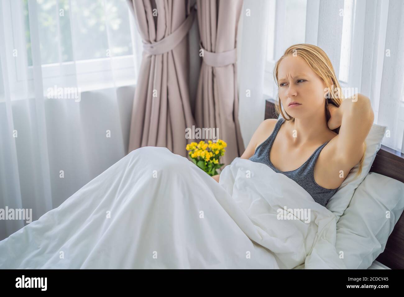 Upset young woman lying in bed in morning feels pain in neck after