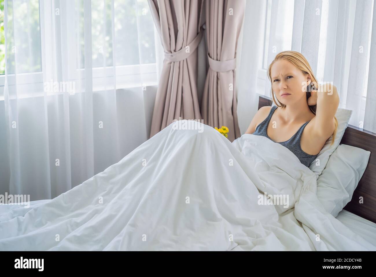Upset young woman lying in bed in morning feels pain in neck after