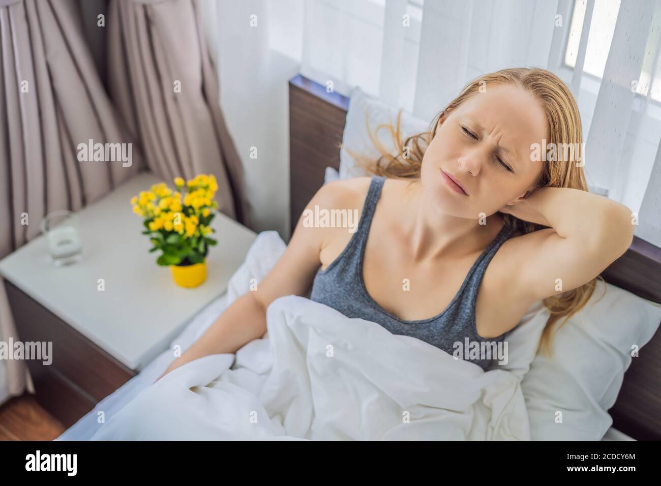 Upset young woman lying in bed in morning feels pain in neck after