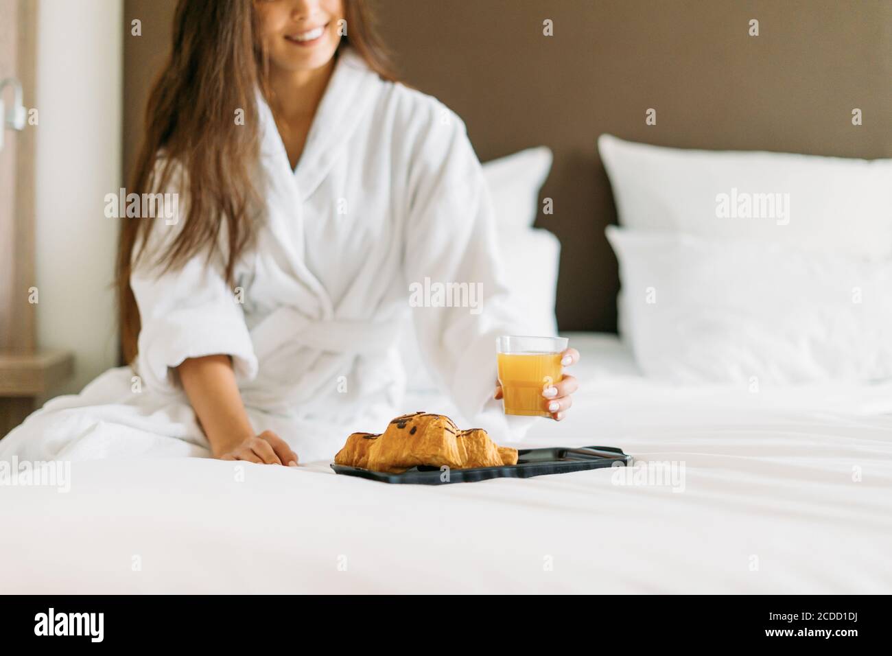 Young smiling woman in white robe having breakfast orange juice and ...