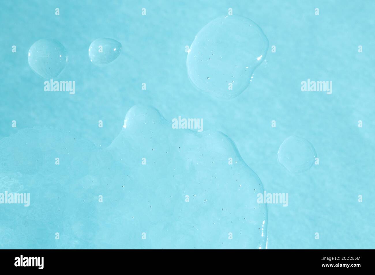 Squeezed cosmetic clear cream gel texture. Close up photo of transparent drop of skin care product. High Quality transparent gel with bubbles closeup on blue background. Stock Photo