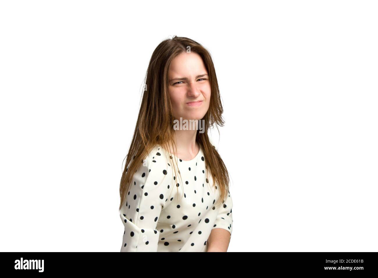 A young woman with long brown hair and a white polka-dot dress. with a displeased expression on her face, she is not happy Stock Photo