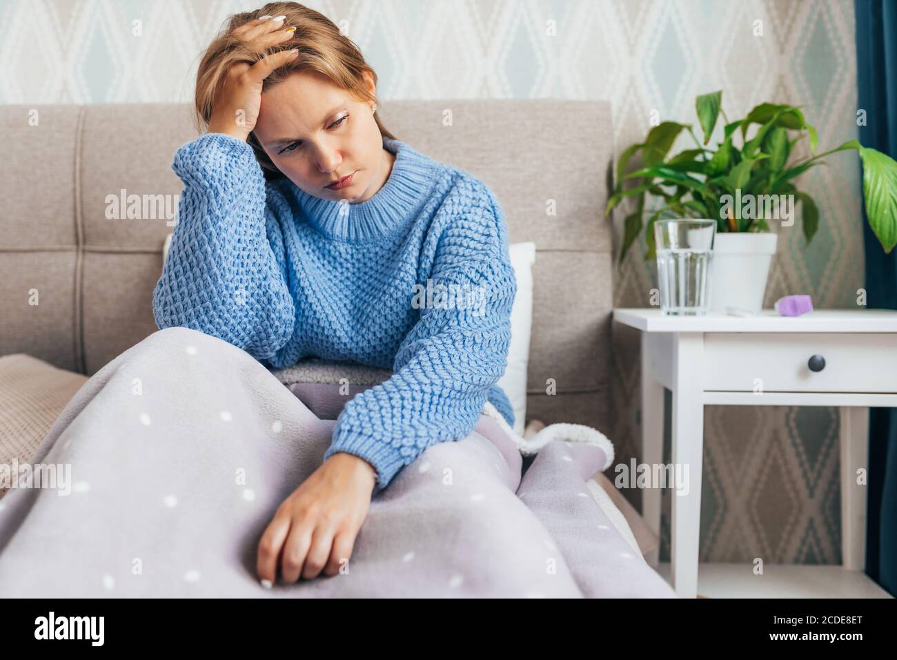 Young blonde woman suffering of depression sitting n bed on in warm sweater. Loneliness, sadness, divorse Stock Photo