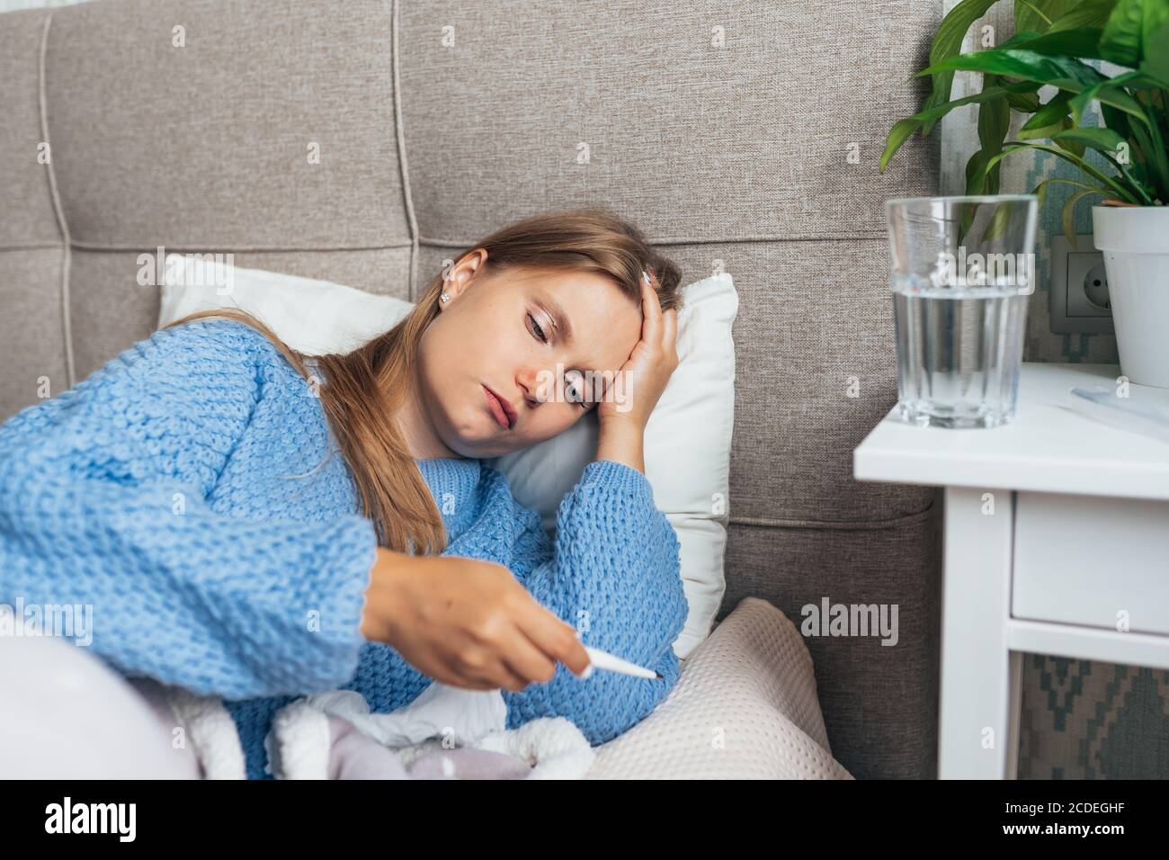 Sick woman with thermometer lying in bed under blanket. Headache, flu, cold, virus Stock Photo