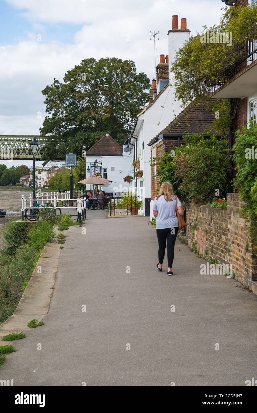 Lone woman walking towards The Bulls Head, a historic 18th century inn on the riverside at Strand-on-the-Green, Chiswick, London,England, UK. Stock Photo