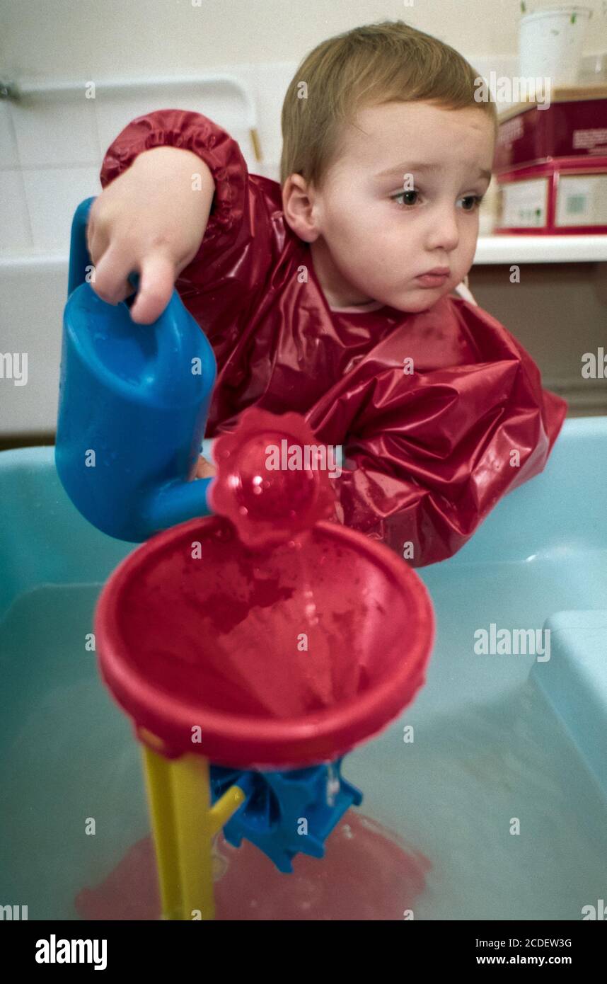 https://c8.alamy.com/comp/2CDEW3G/a-young-boy-pours-water-from-a-plastic-watering-can-into-a-funnel-which-drives-gears-whilst-wearing-an-apron-at-west-hampstead-pre-school-in-london-nw6-25-october-1993-photo-neil-turner-2CDEW3G.jpg