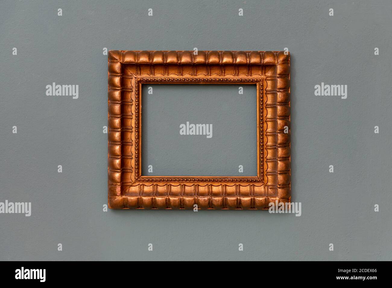 Ornate gold empty frame hanging centered on a green wall with copyspace for an artwork, picture or painting Stock Photo