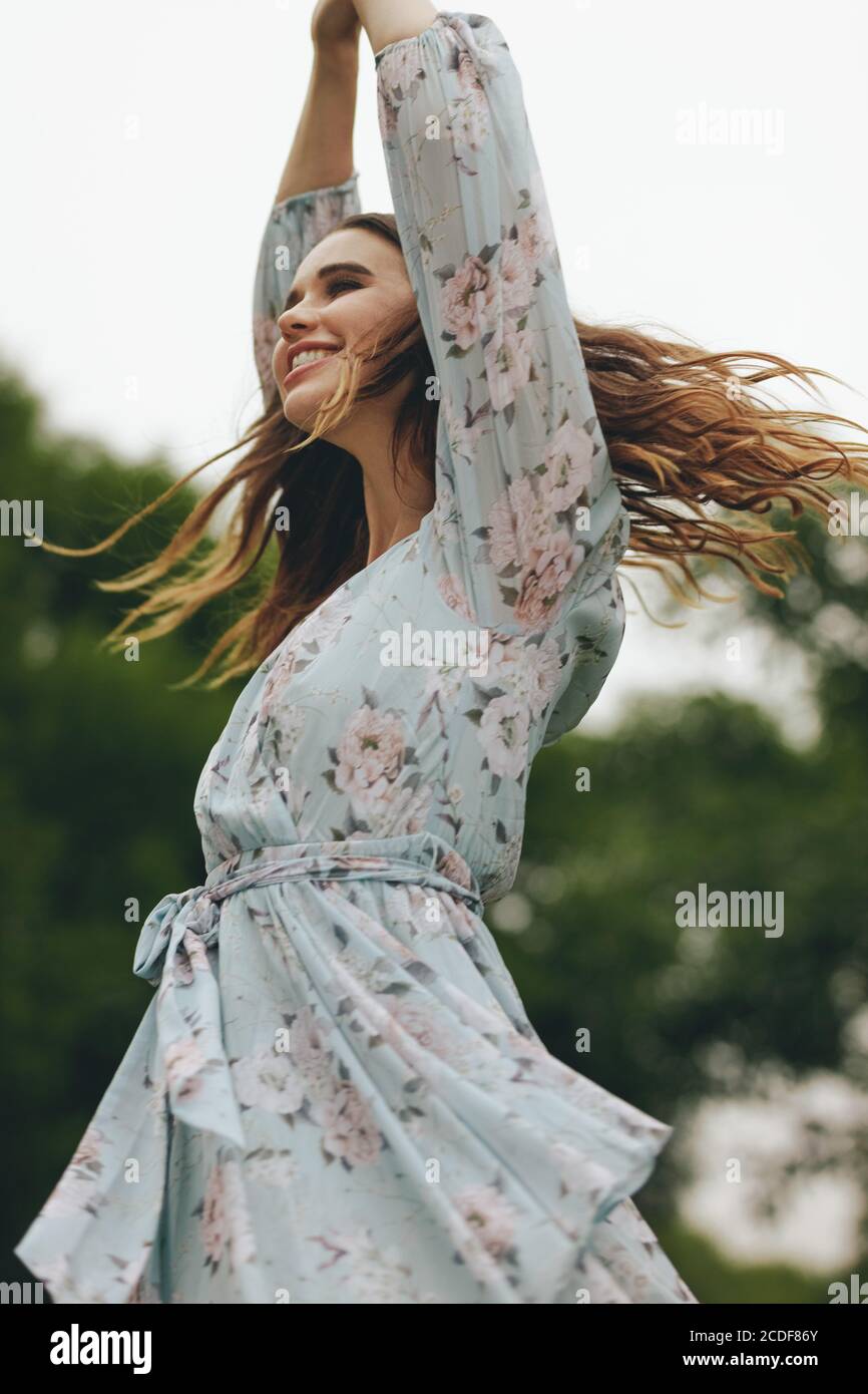 Woman in a floral dress dancing outdoors. Beautiful female dancing and having fun at the park. Stock Photo
