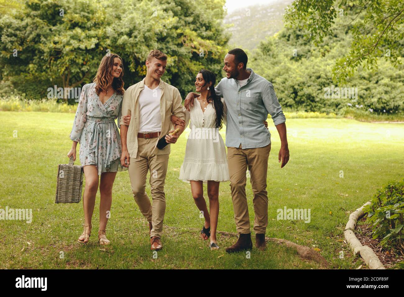 Group of young people walking towards the picnic spot in the park. Smiling couples walking in