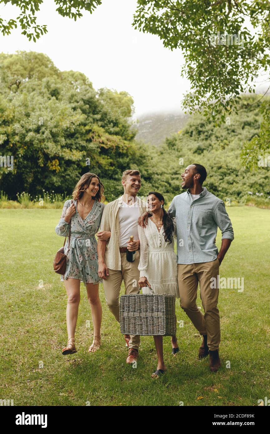 Two young couples walking in the park carrying a picnic basket. Group of friends walking towards the picnic spot in the park. Stock Photo