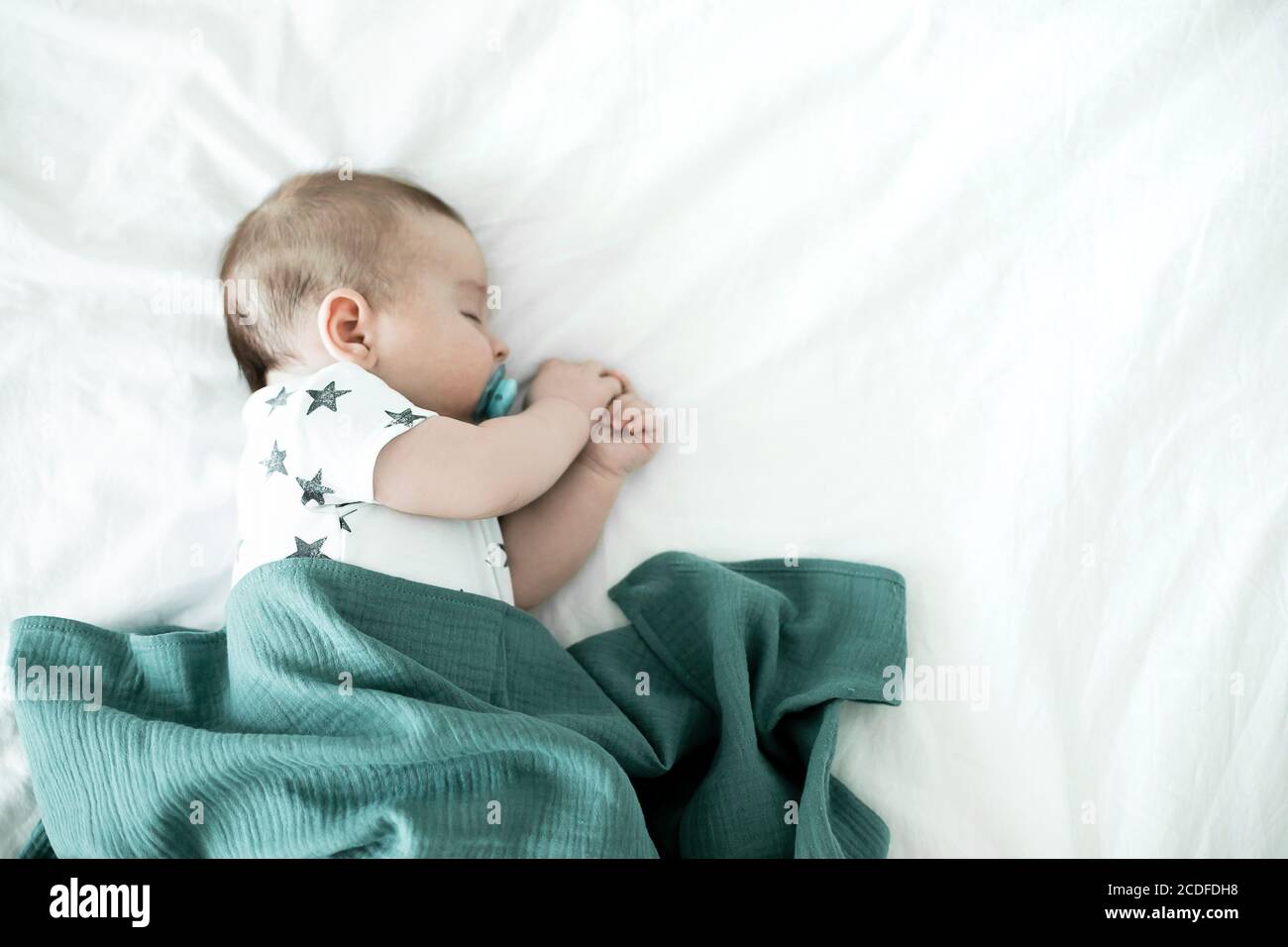 3 month old baby sleeping on bed and covered with a muslin diaper. Top