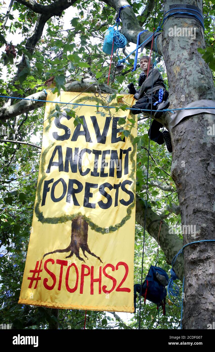 A Stop HS2 campaigner unfurls a banner in trees outside Euston Station in London as activists set up a camp within the trees as part of the wider Extinction Rebellion weekend of action across the country. Stock Photo