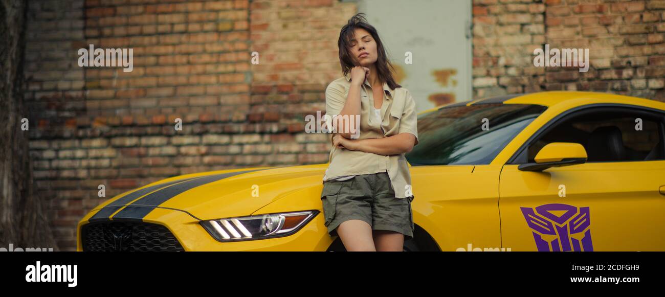 Girl stands near yellow car with the autobot logo or robot transformer. Stock Photo