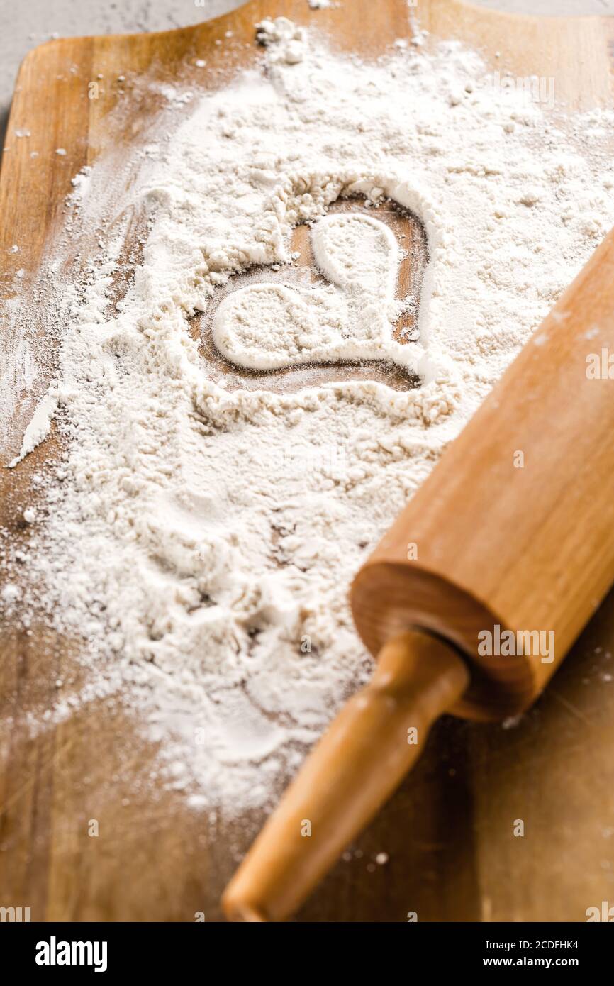 Rolling pin with heart shape in flour on wooden cutting board. Love