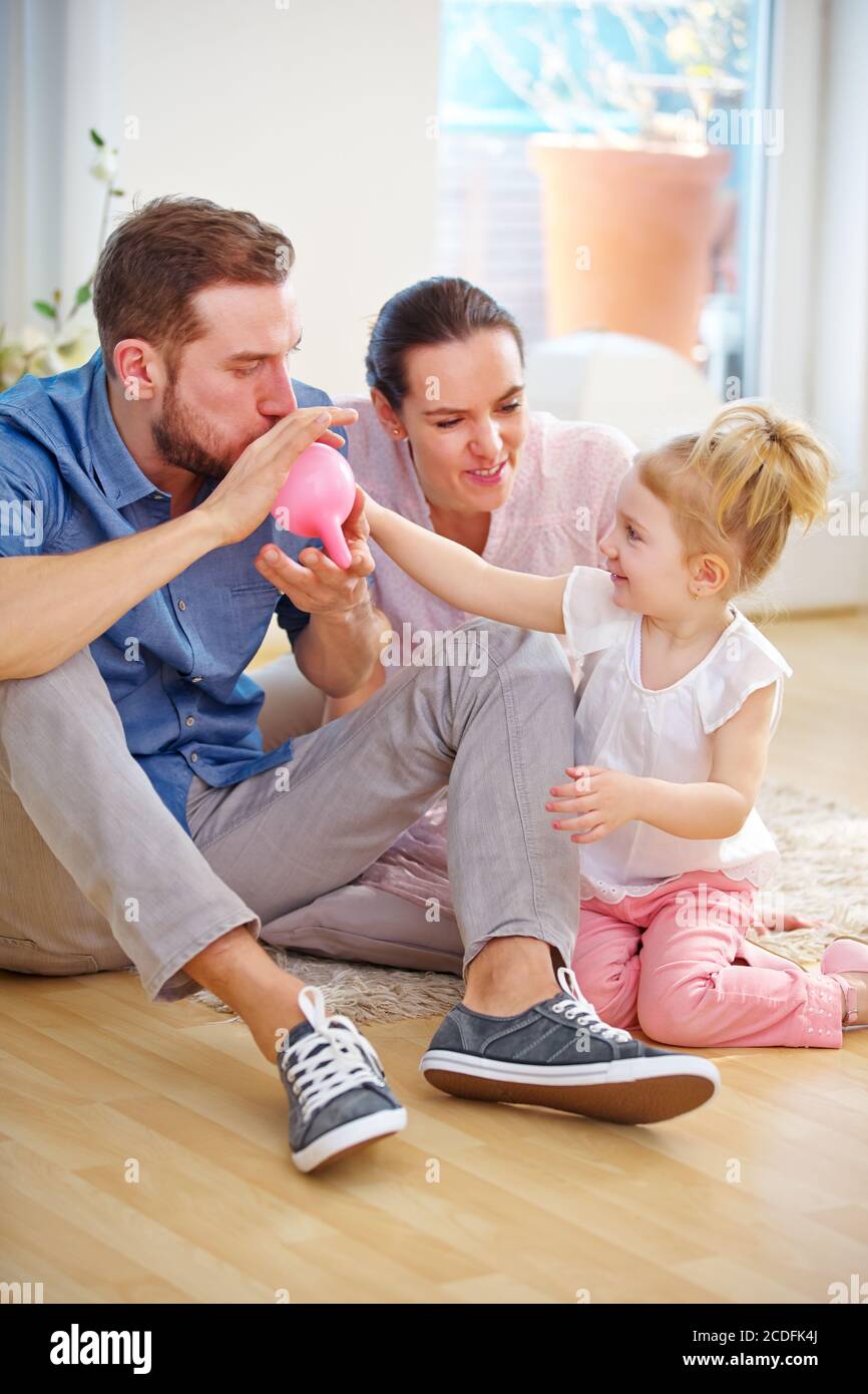 Family with child has fun blowing up a balloon at home Stock Photo