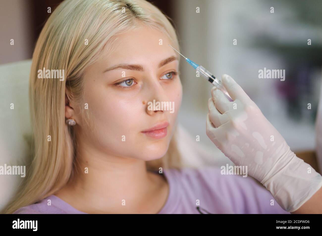 Hands of cosmetologist making injection in face, lips. Young woman gets