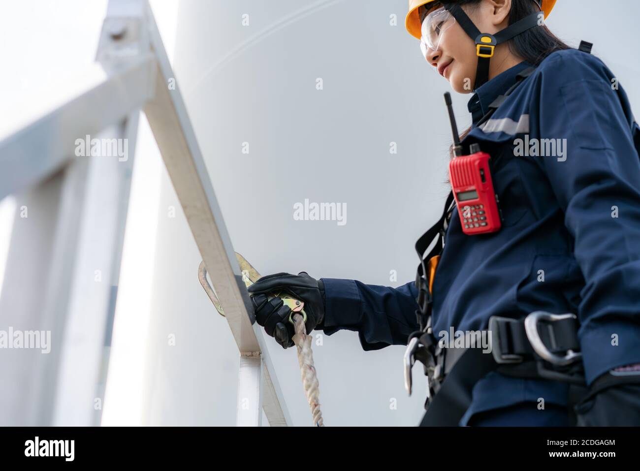 Asian woman Inspection engineer wearing safety harness and safety line working preparing and progress check of a wind turbine with safety in wind farm Stock Photo