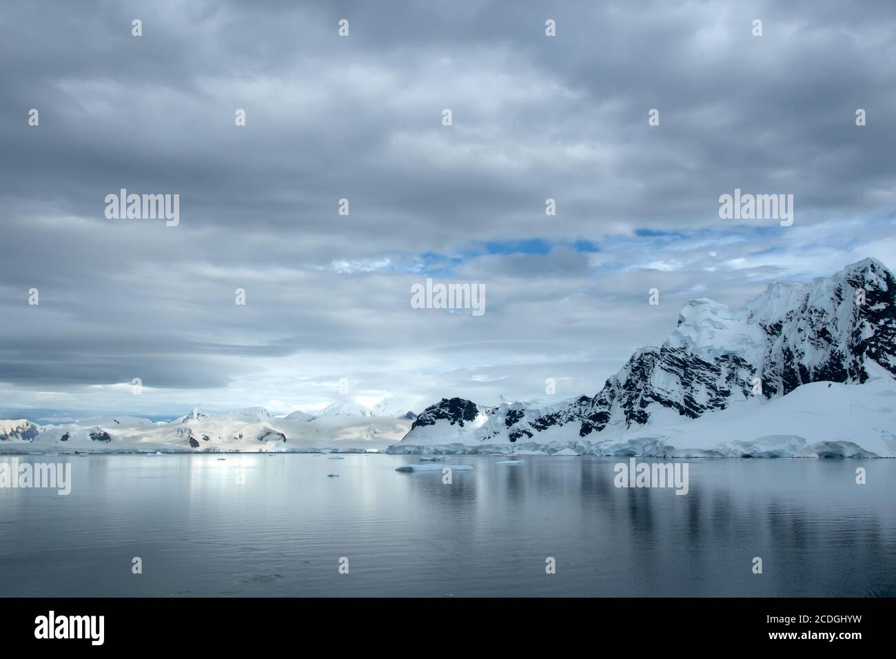 Mountain range in Antarctica covered in snow and ice with icebergs floating in the ocean Stock