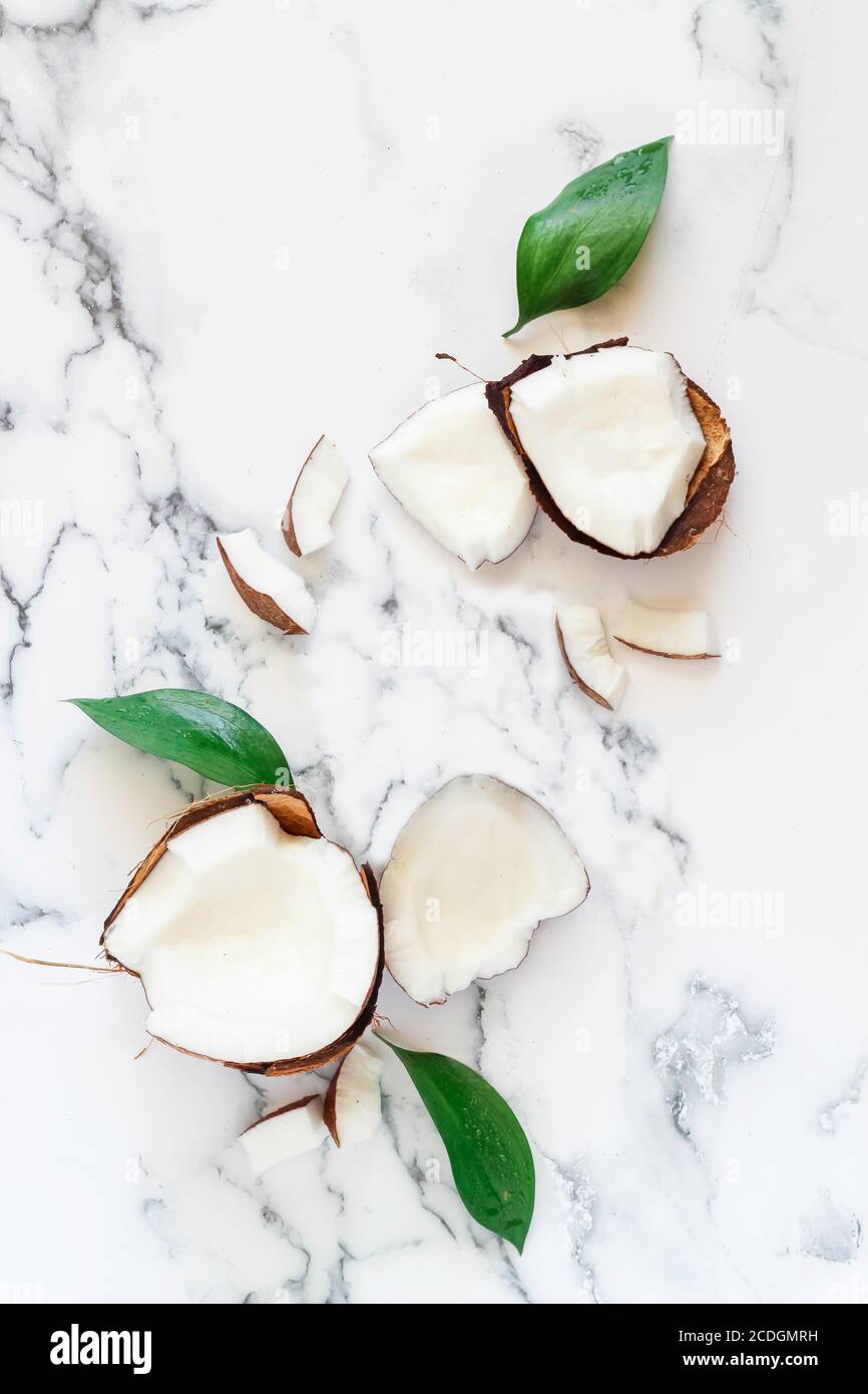 Flatlay with broken coconut and green leaves on a white marble background. Mock up for health and beauty products advertising Stock Photo