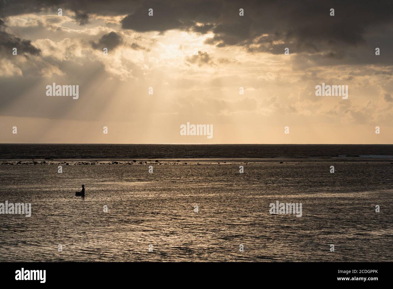 Ray of light above the shore broke through the black clouds. The sea is golden in color, and the atmosphere is quiet and serene. A sailor is looking f Stock Photo