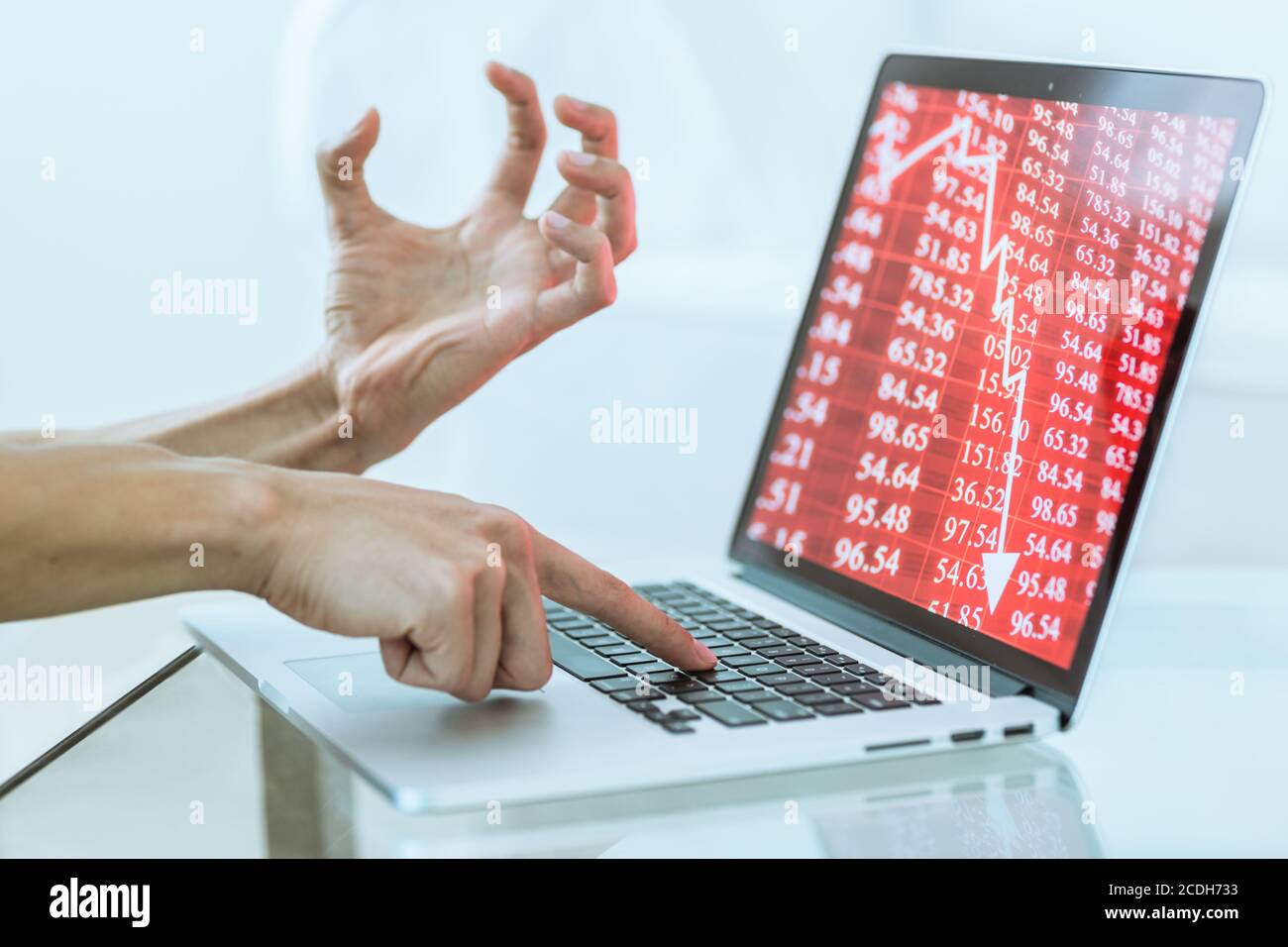 Stressed hand gesture of investor losing money in the stock market crash while typing on a laptop computer. Economy falling red chart. Close-up. Stock Photo