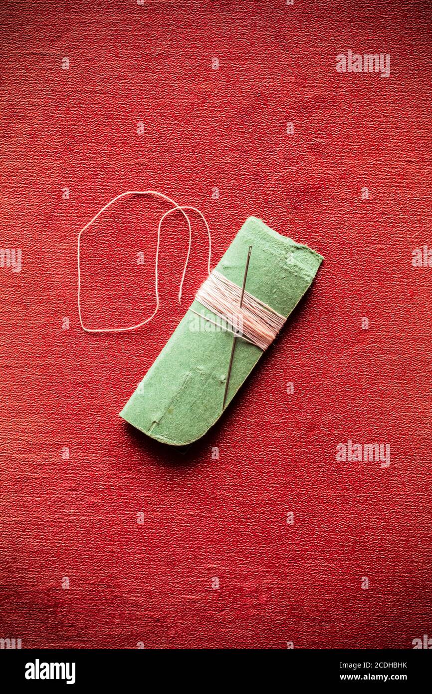 A needle and pink thread wrapped around a piece of green card, on a red background Stock Photo