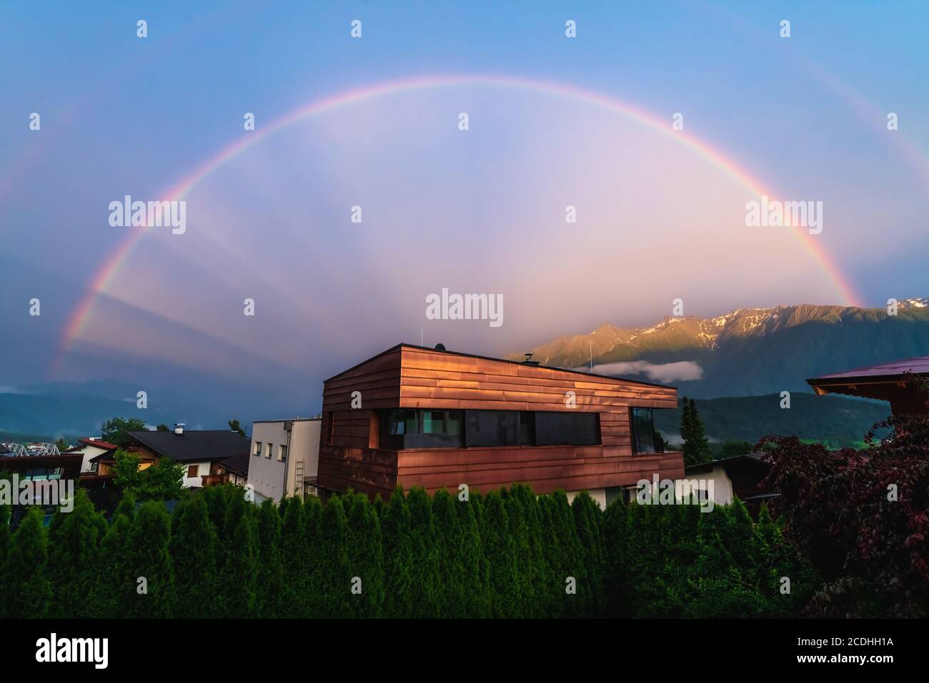 Scenic full Rainbow over modern copper building in Austrian alp mountains village during sunset, Wildermieming, Mieminger Plateau, Tyrol, Austria Stock Photo
