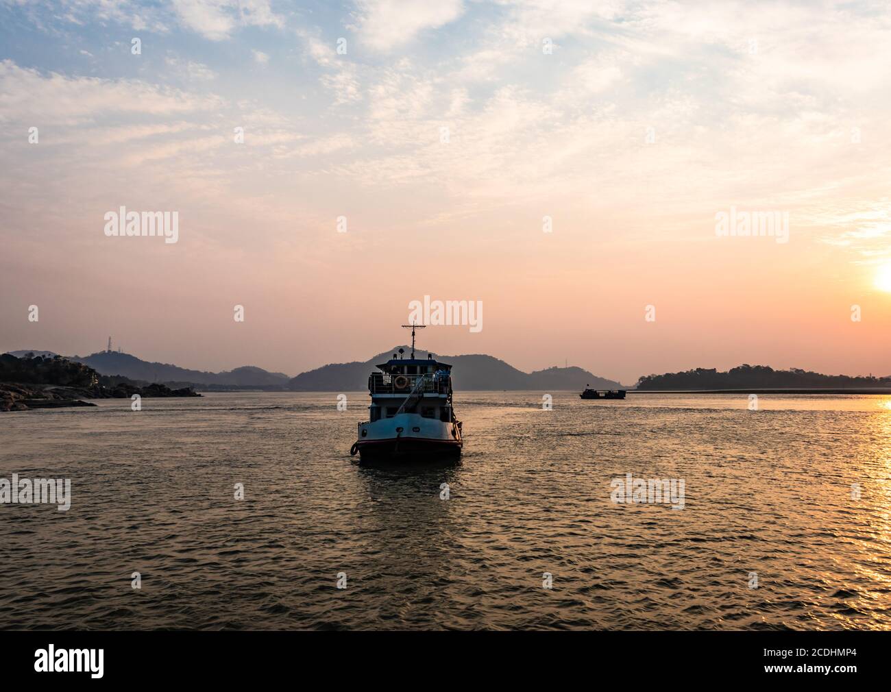 ship heading towards river island at dusk image is taken at peacock island guwahati assam india. it is showing the serene beauty of nature at dusk. Stock Photo