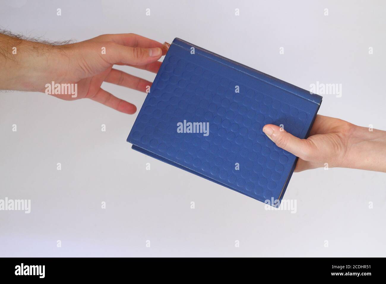 One hand passing a book to another hand. Isolated against a white
