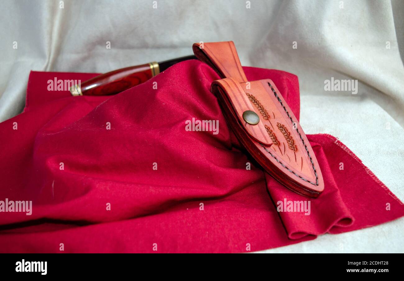 A uniquely decorated leather sheath is displayed on a red fabric while the knife sits in the background with a bokeh effect to draw attention to the s Stock Photo