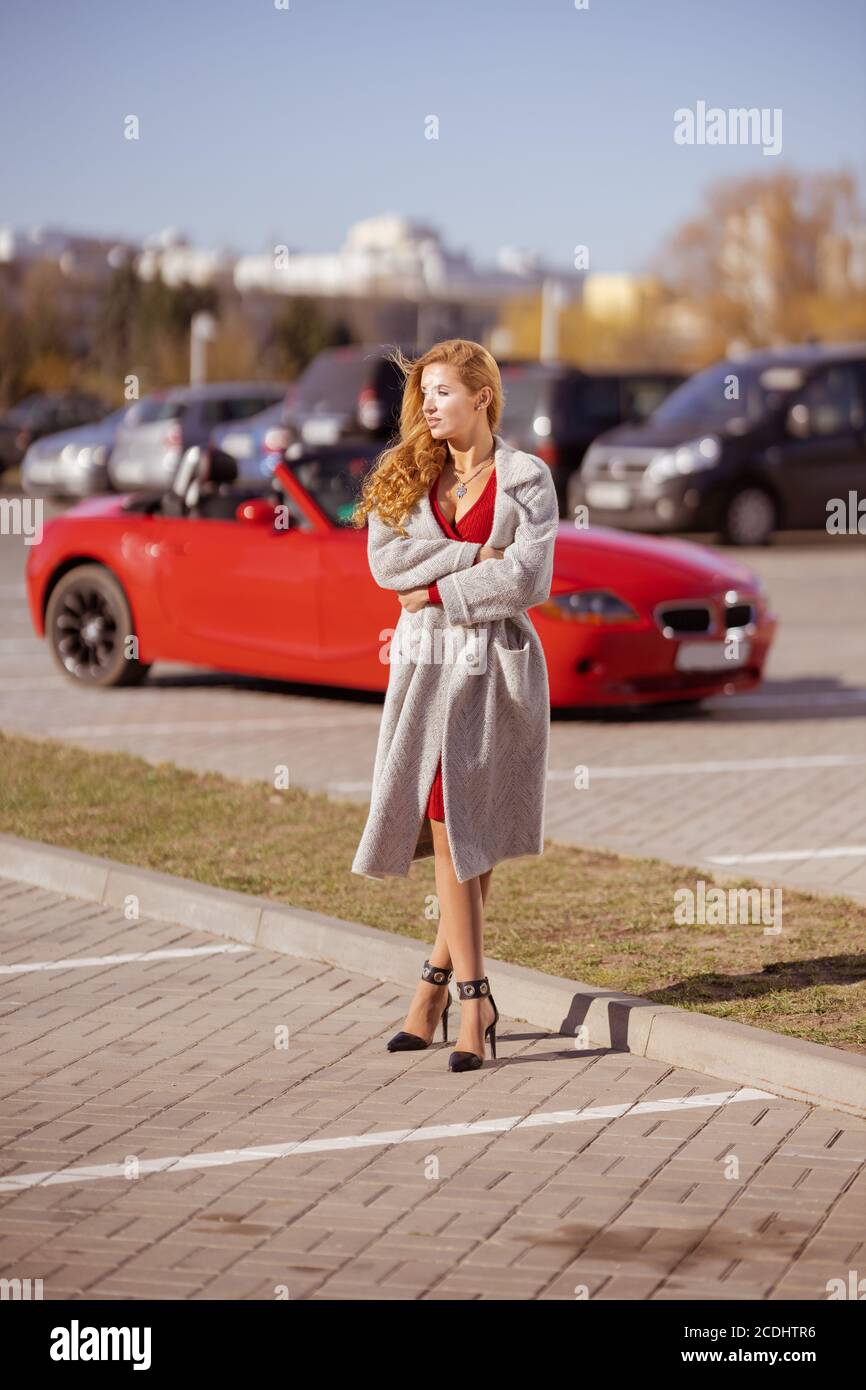Beautiful blonde woman in a red dress posing in a red car in the city on a sunny day Stock Photo
