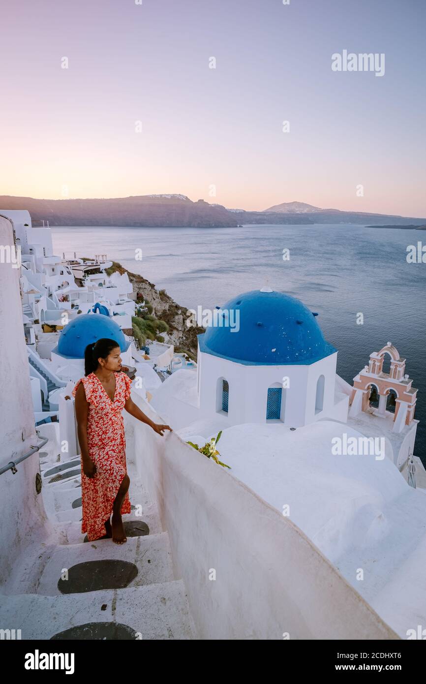 Santorini Greece, young woman on luxury vacation at the Island of Santorini watching sunrise by the blue dome church and whitewashed village of Oia Stock Photo