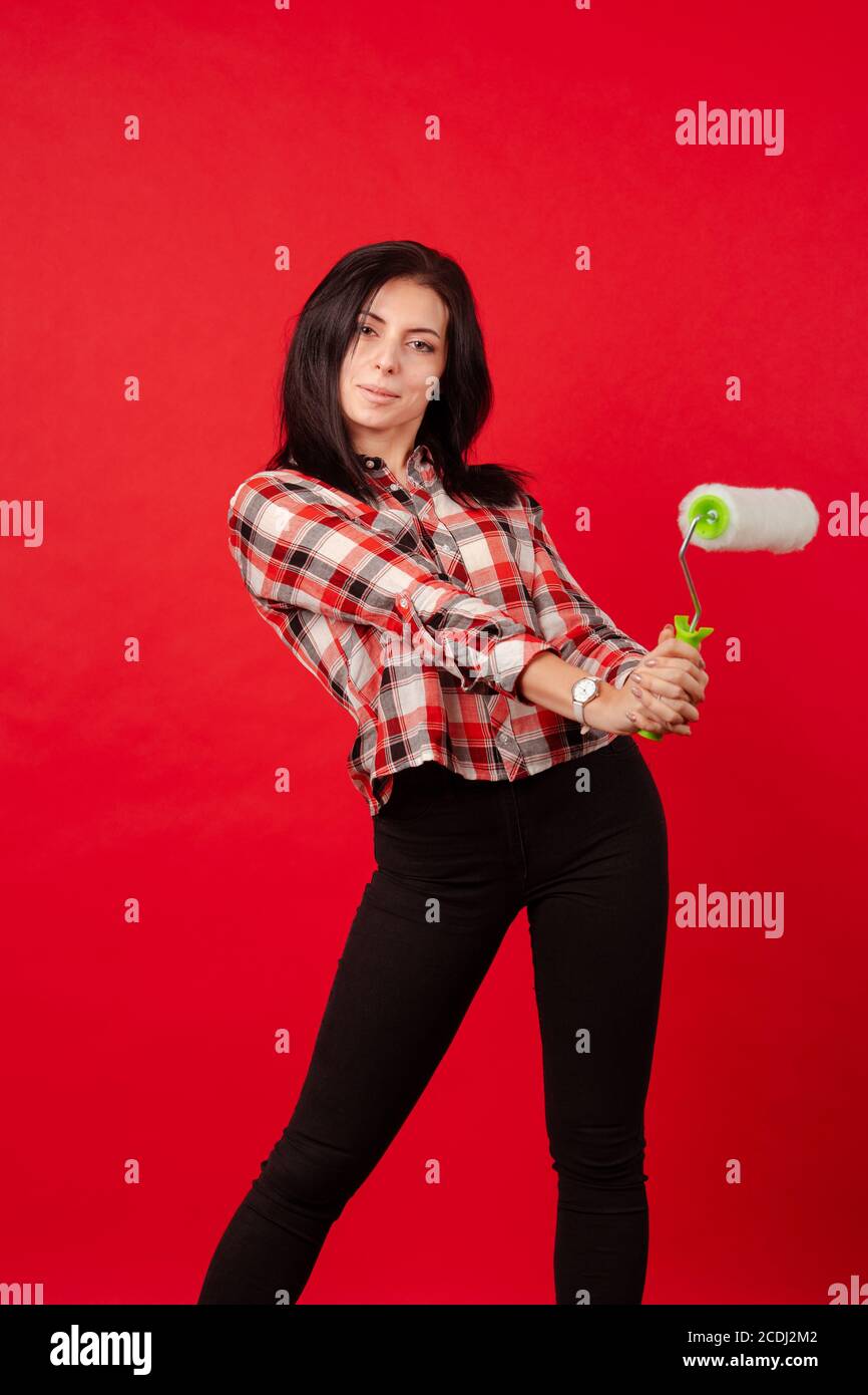 Girl master builder painter in a plaid shirt with a roller for painting  poses on a red background Stock Photo - Alamy