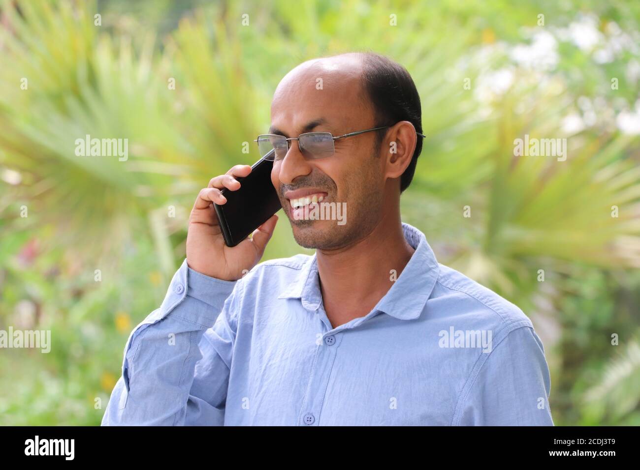 Smiling Asian man talking on mobile phone outside in a park Stock Photo