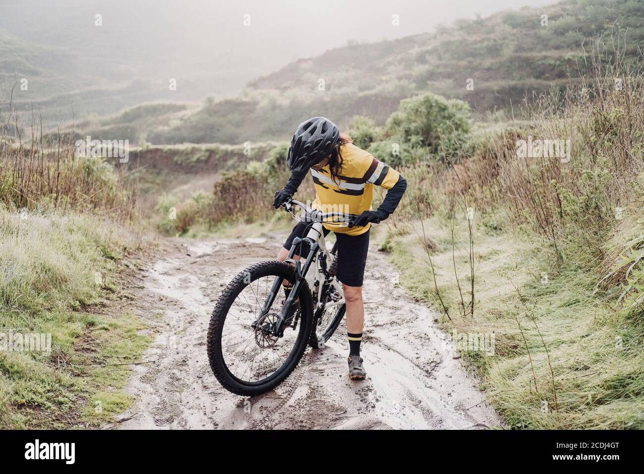 Full body of female cyclist on muddy mountain path on rainy day Stock Photo