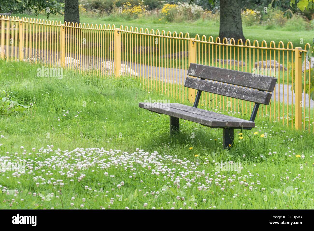 Overgrown solitary public seat / bench in a kid's playground empty of people during UK Covid lockdown. Deserted public space, empty park bench in UK. Stock Photo