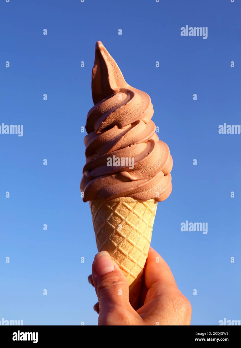 Hand Holding a Chocolate Soft Serve Ice Cream Cone Against Sunny Blue